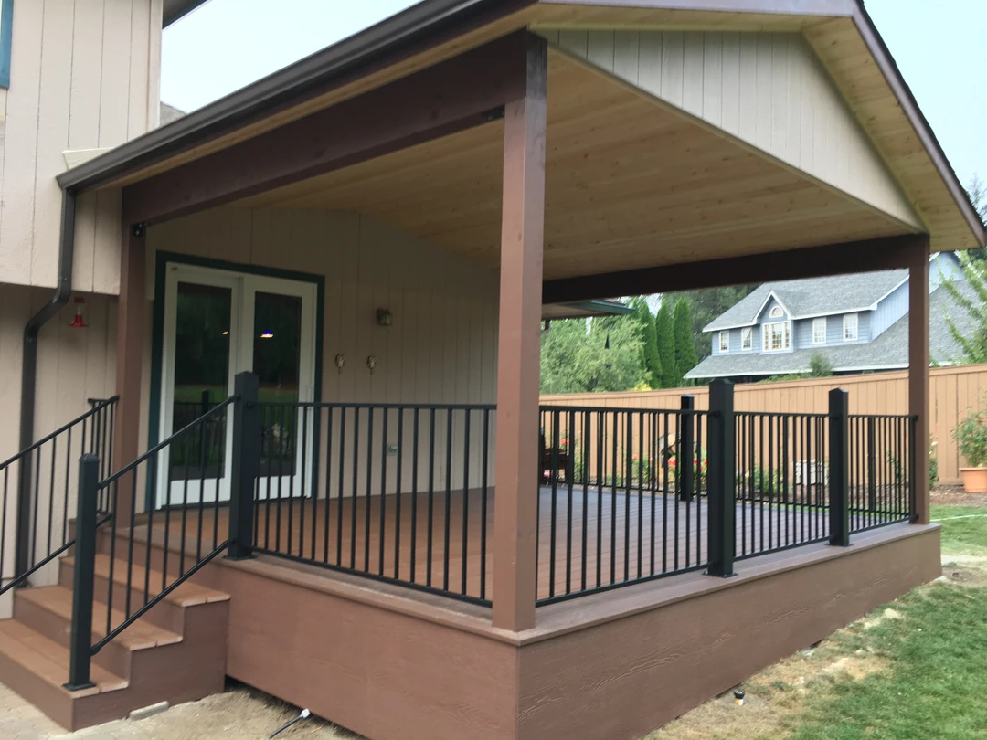 Covered porch with wood ceiling, black railing, and deck stairs